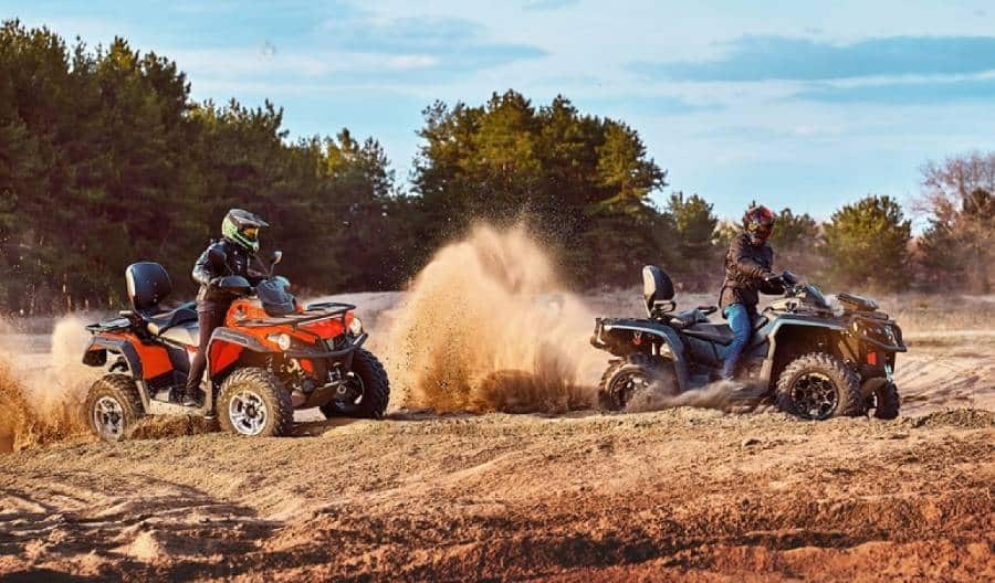 Two people riding ATVs in a dirt field, demonstrating how to change ATV brake pads.